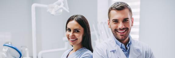 Zahnarzt und Assistenzärztin stehen Rücken an Rücken und lächeln